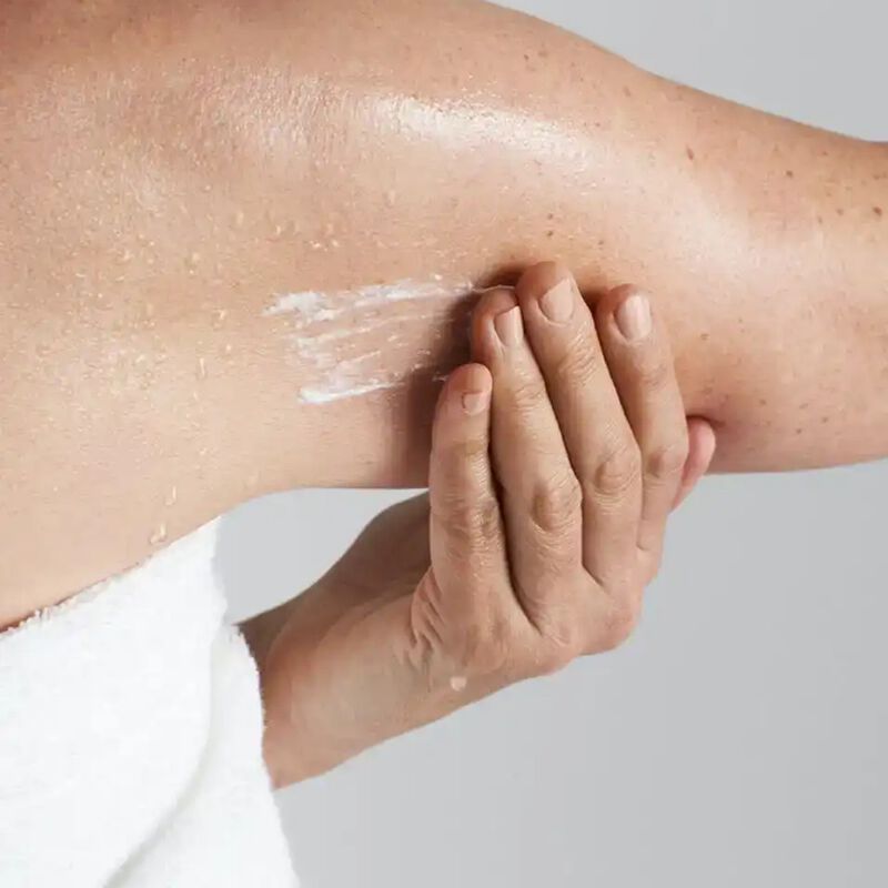 Person massaging Crepe Control™ Body Cream into arm after using the body scrub
